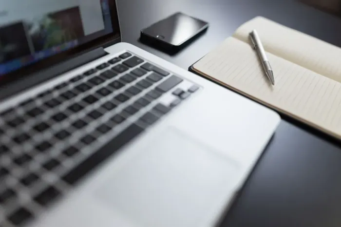 Profesional mencatat hasil kerja harian di buku catatan dekat laptop
