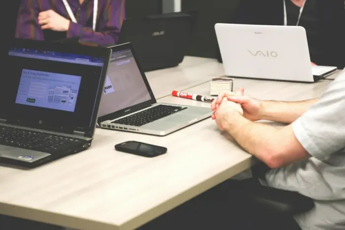 Tangan menyunting draf tulisan di meja dengan laptop dan pena.